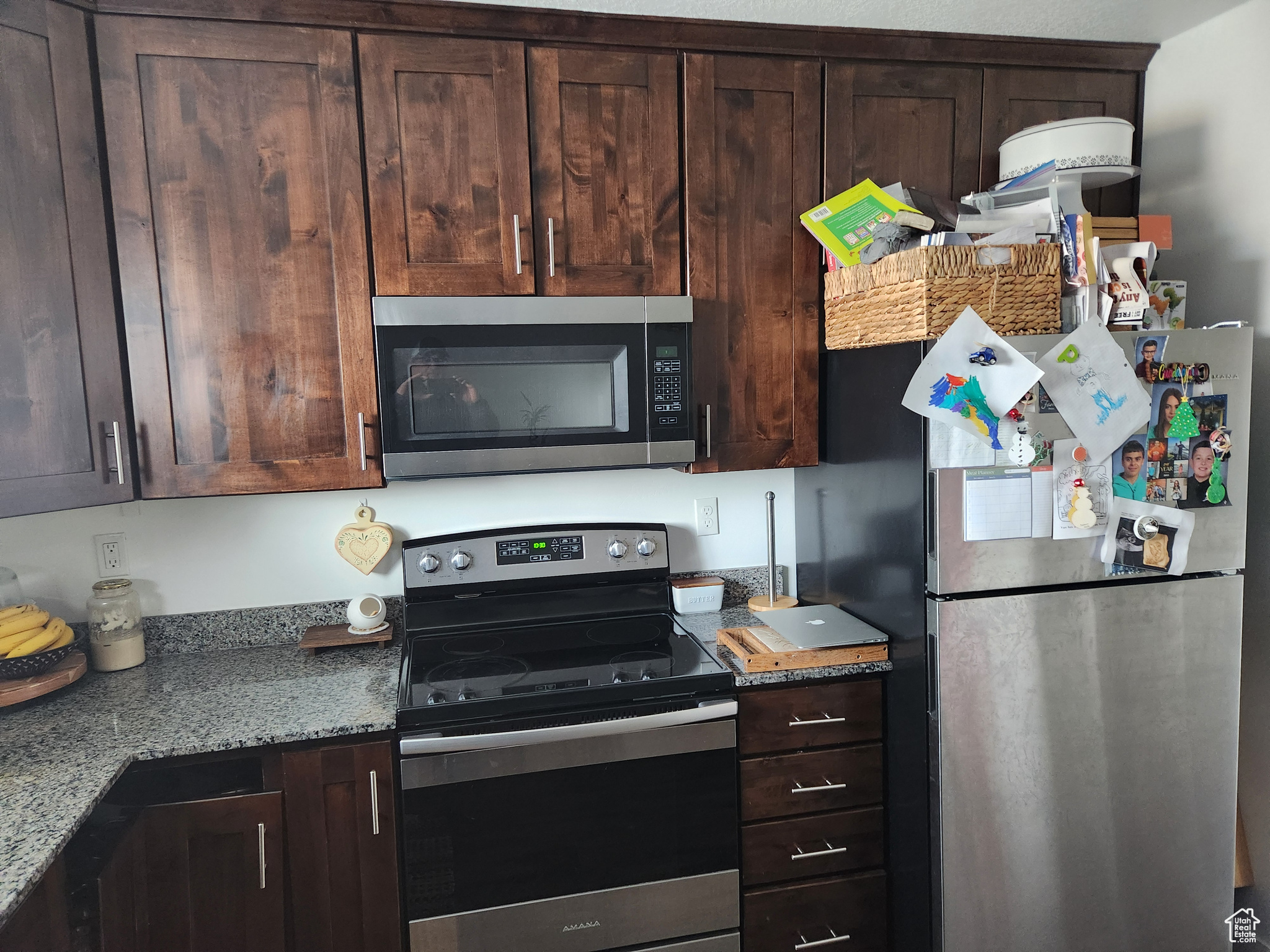 Kitchen featuring dark brown cabinetry, appliances with stainless steel finishes, and light stone countertops