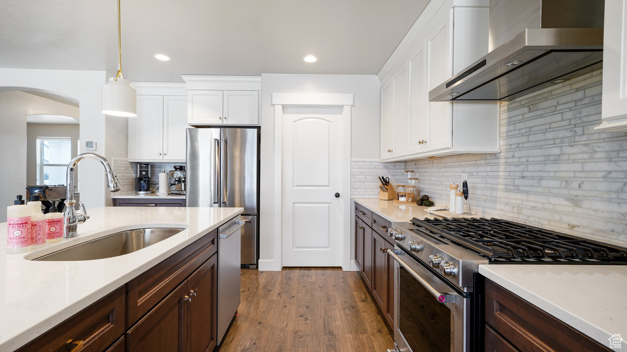 Kitchen with decorative light fixtures, white cabinetry, sink, high end appliances, and wall chimney range hood