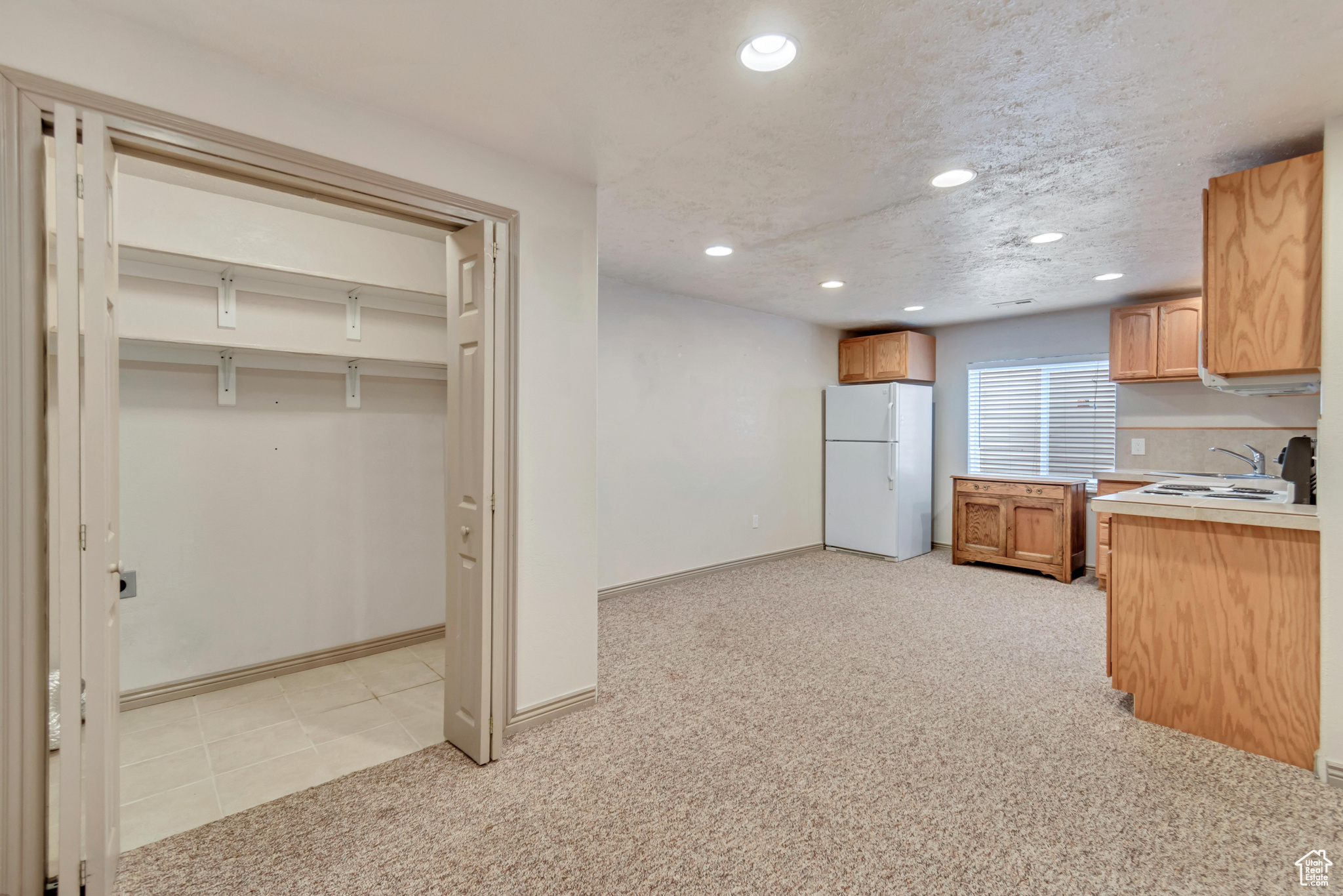 Kitchen featuring light colored carpet, sink, white fridge, and a textured ceiling