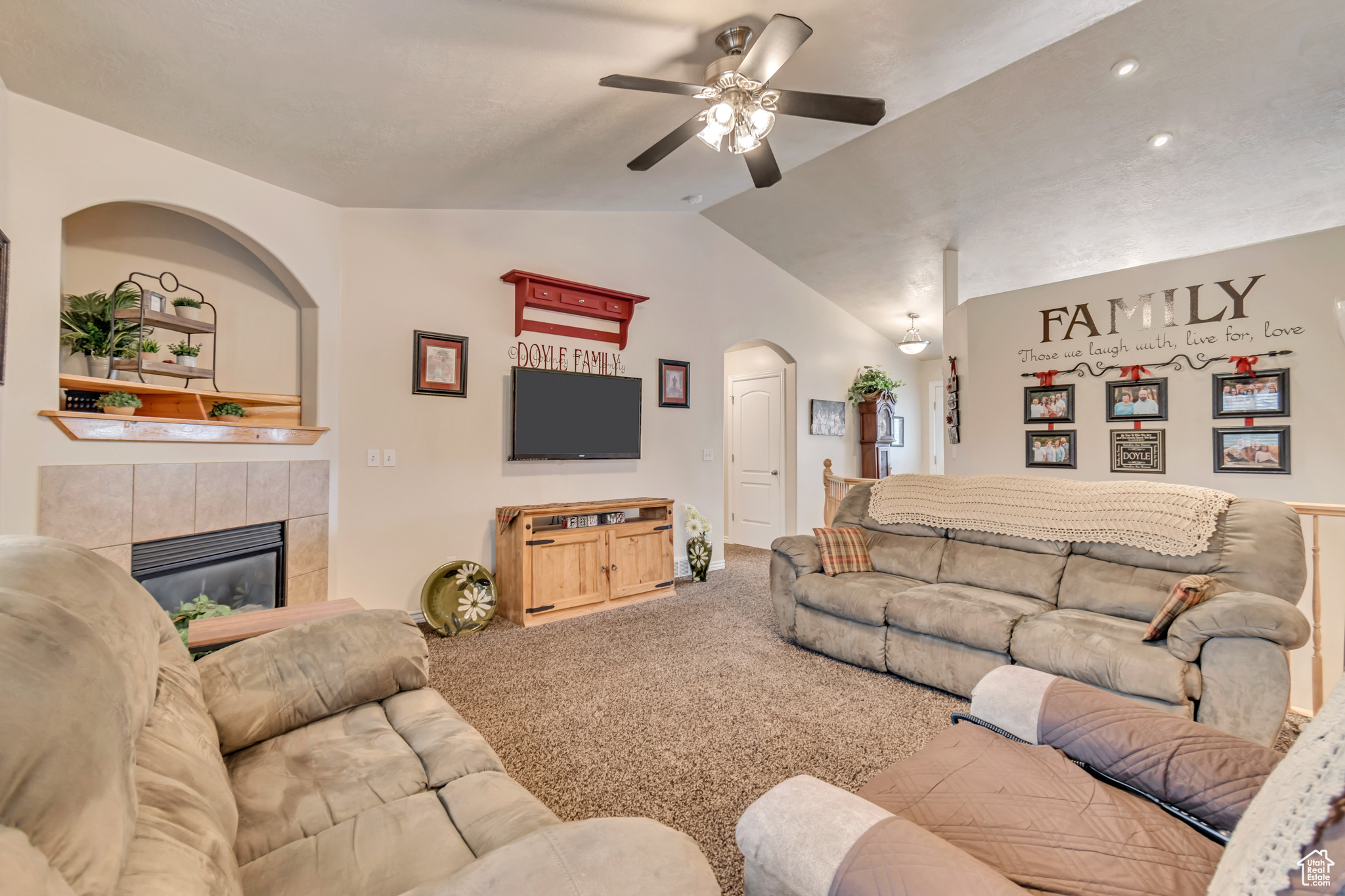 Carpeted living room featuring a tile fireplace, lofted ceiling, and ceiling fan