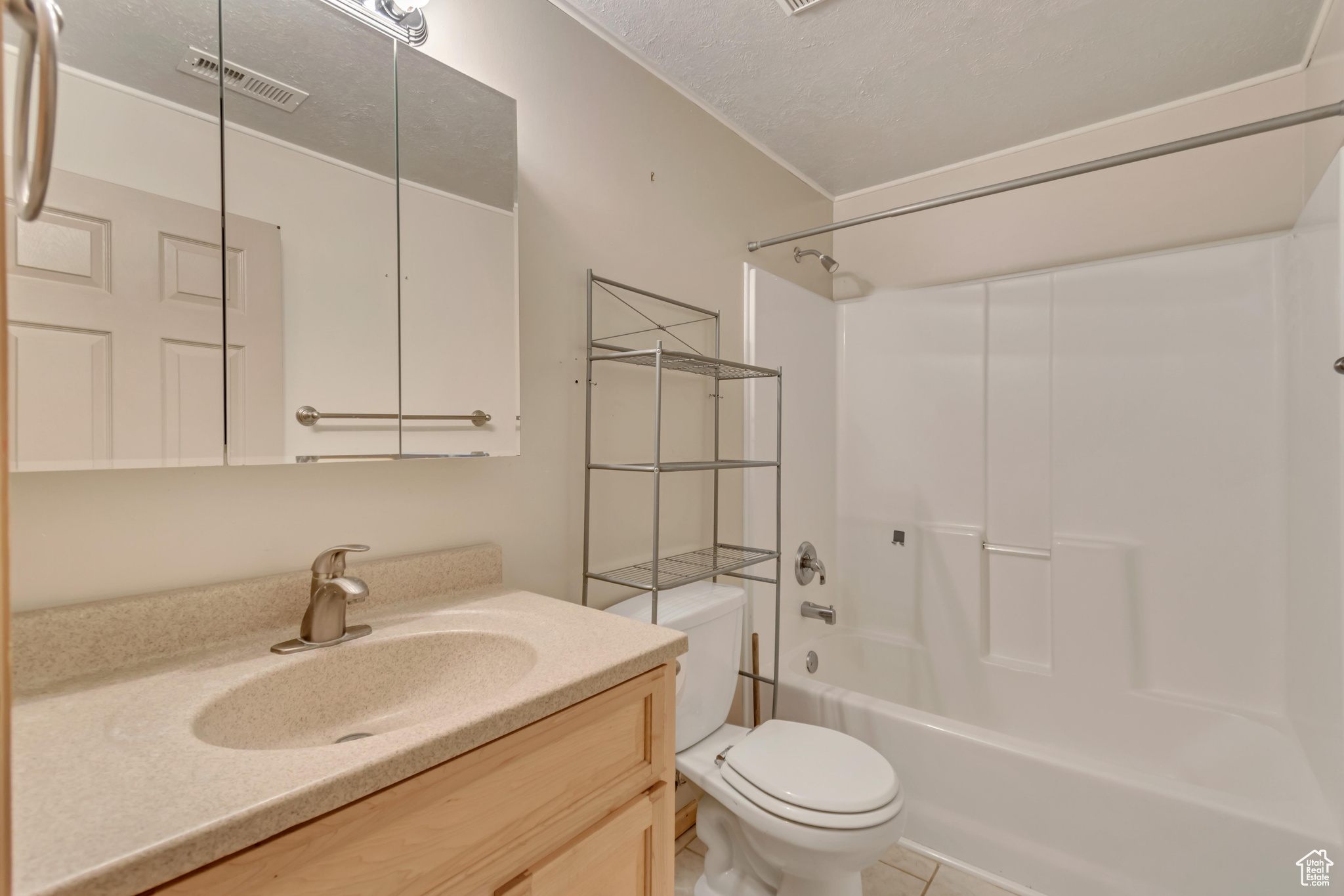 Full bathroom with  shower combination, vanity, a textured ceiling, tile patterned floors, and toilet