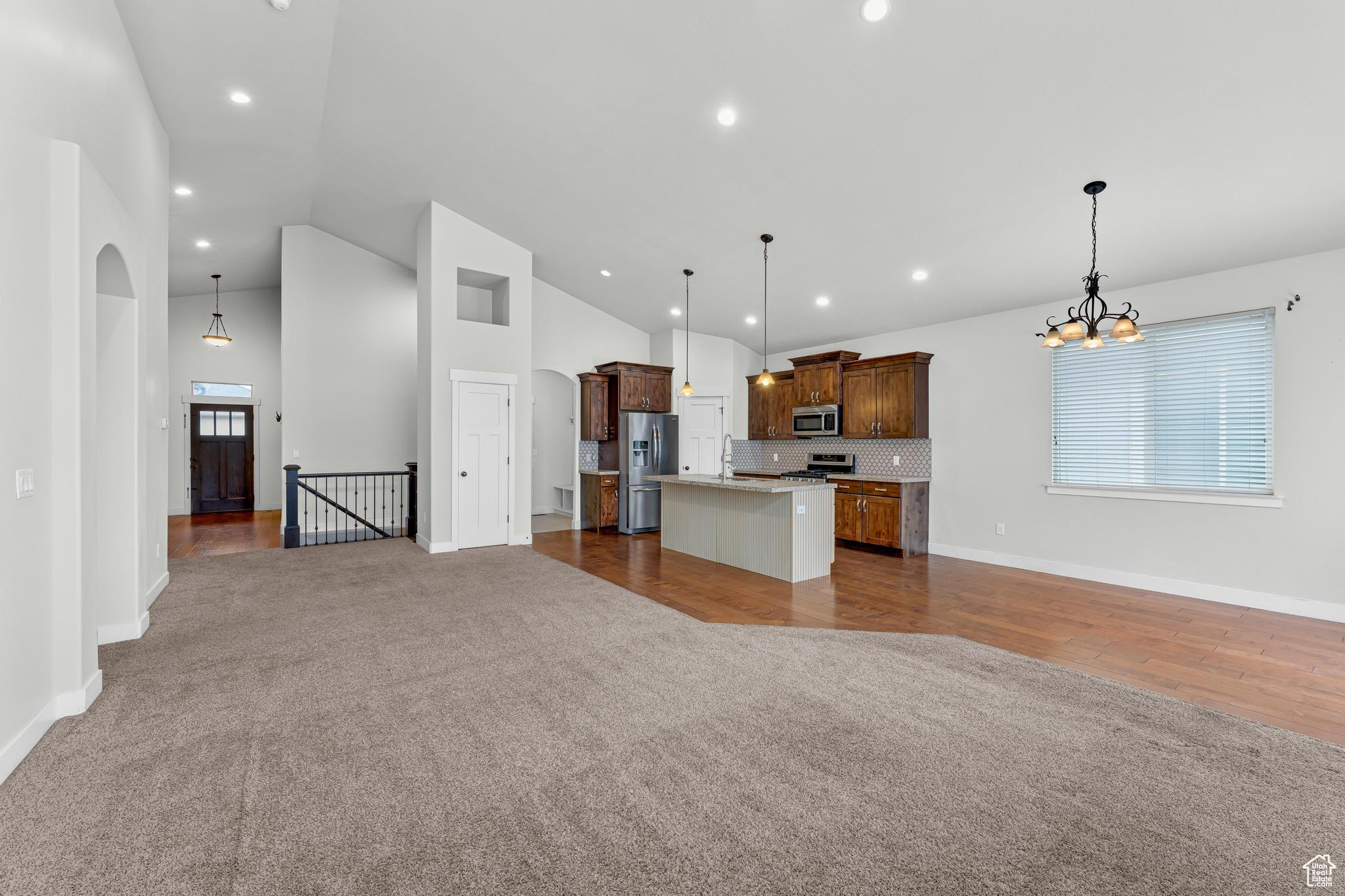 Pendant lighting, a center island, carpet flooring, and appliances with stainless steel finishes