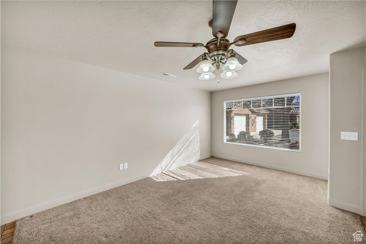 Spare room with ceiling fan, light colored carpet, and a textured ceiling