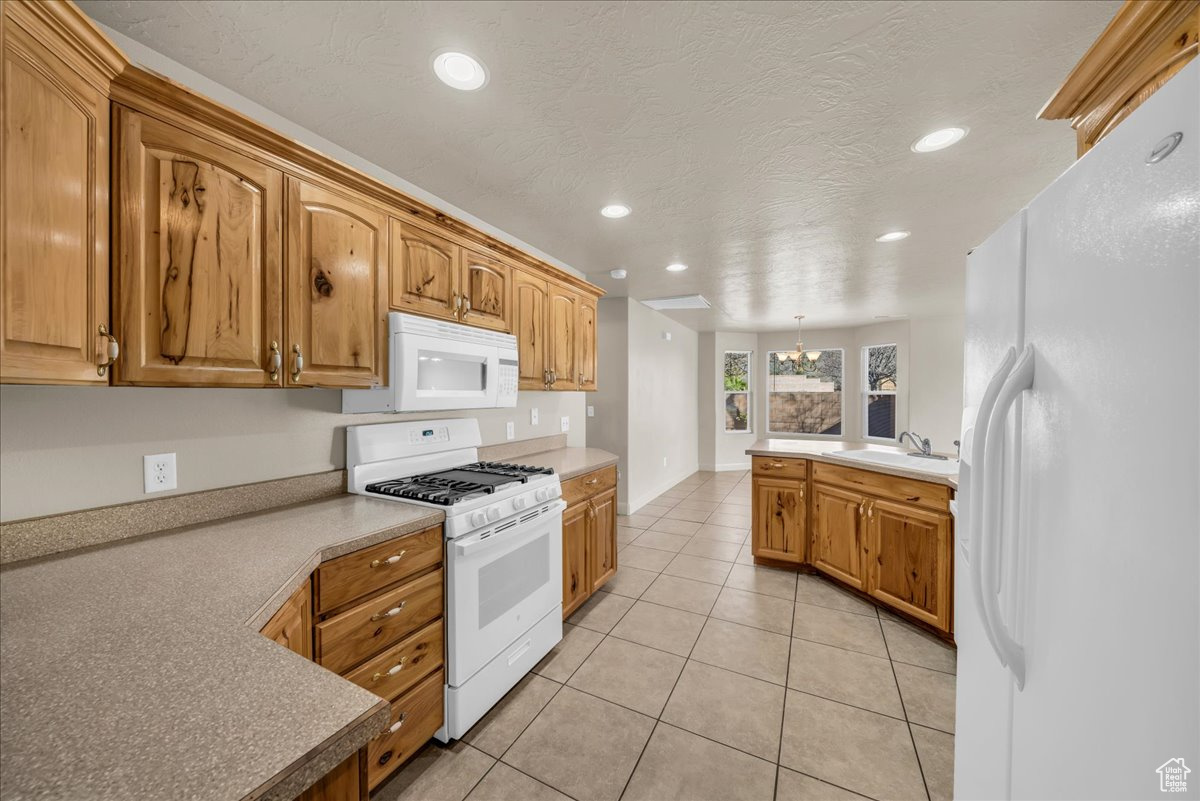 Kitchen featuring sink, white appliances, light tile patterned flooring, decorative light fixtures, and a chandelier