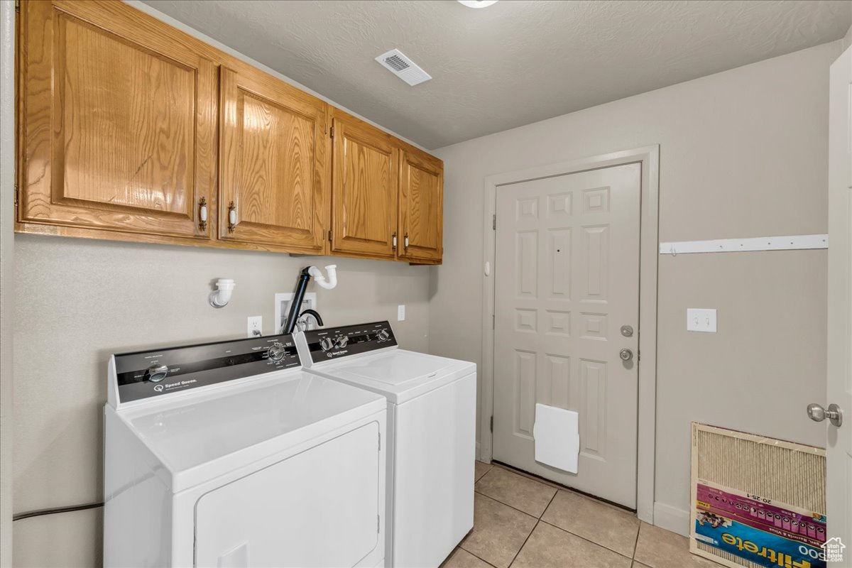 Washroom with cabinets, light tile patterned flooring, a textured ceiling, and washer and clothes dryer