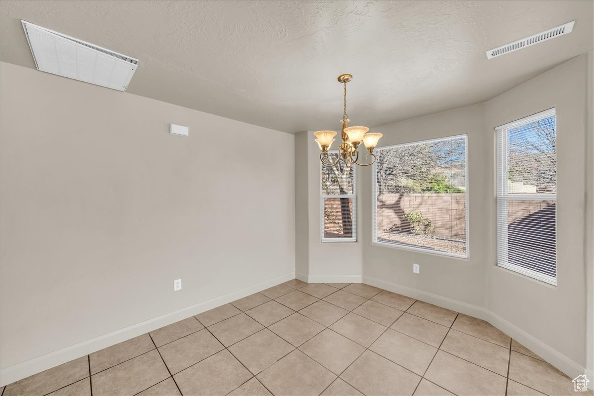 Unfurnished dining area with light tile patterned floors, a notable chandelier, and a textured ceiling