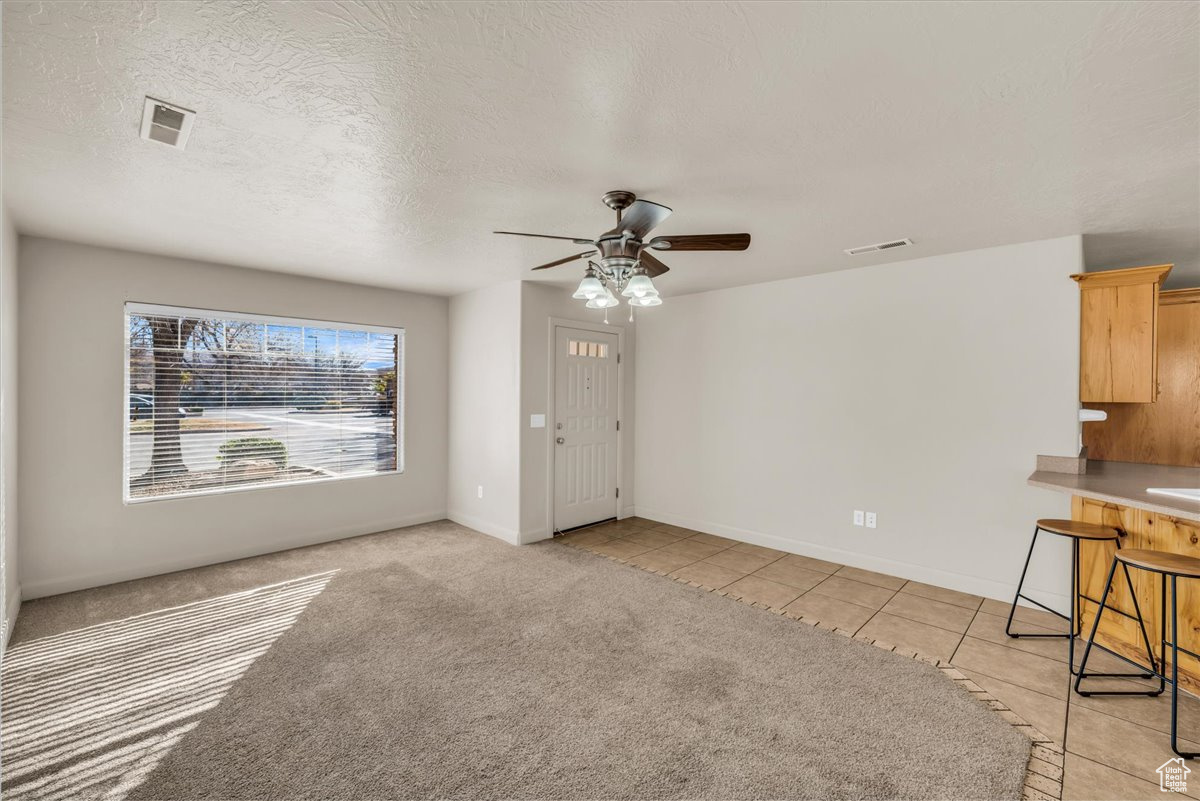 Unfurnished living room with ceiling fan, light carpet, and a textured ceiling