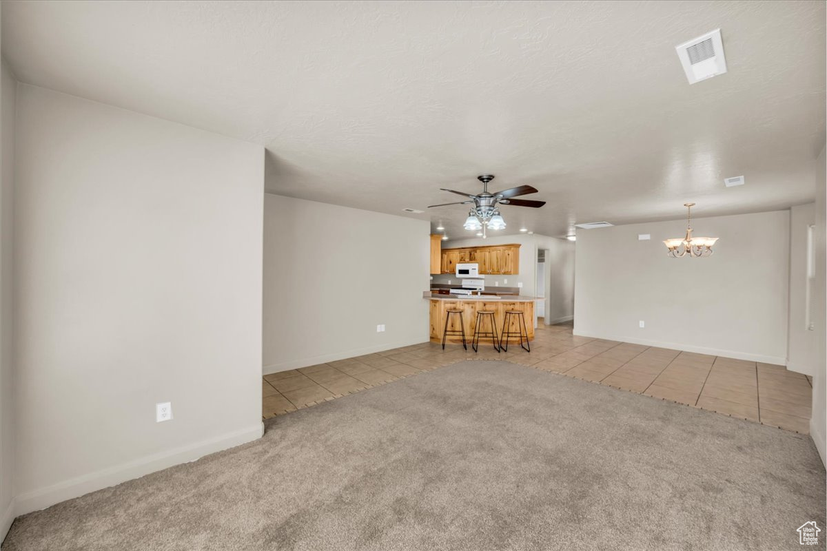 Unfurnished living room with ceiling fan with notable chandelier, light colored carpet, and a textured ceiling