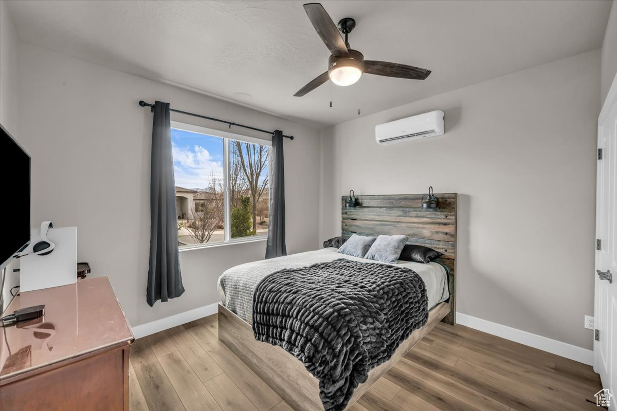 Bedroom with a wall mounted air conditioner, hardwood / wood-style floors, and ceiling fan