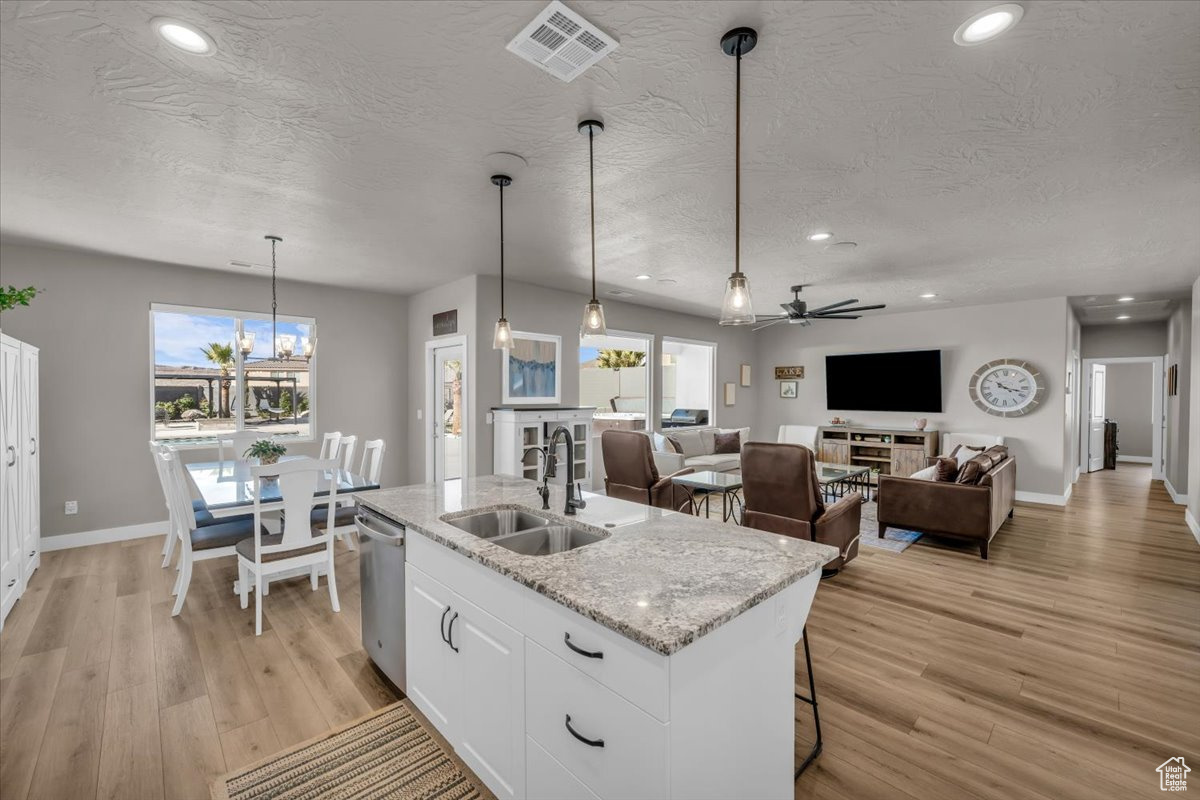 Kitchen featuring pendant lighting, sink, white cabinetry, a kitchen island with sink, and light stone countertops