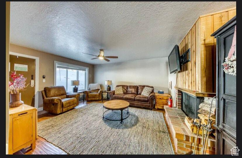 Living room with hardwood / wood-style flooring, ceiling fan, a brick fireplace, and a textured ceiling