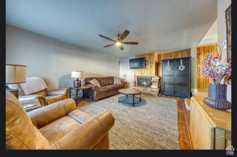 Living room with hardwood / wood-style flooring, ceiling fan, a textured ceiling, and wood walls