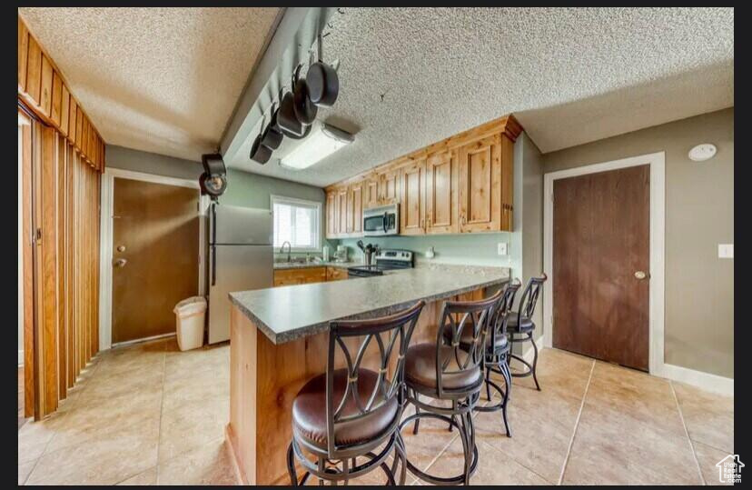 Kitchen with light tile patterned floors, sink, stainless steel appliances, a kitchen bar, and kitchen peninsula