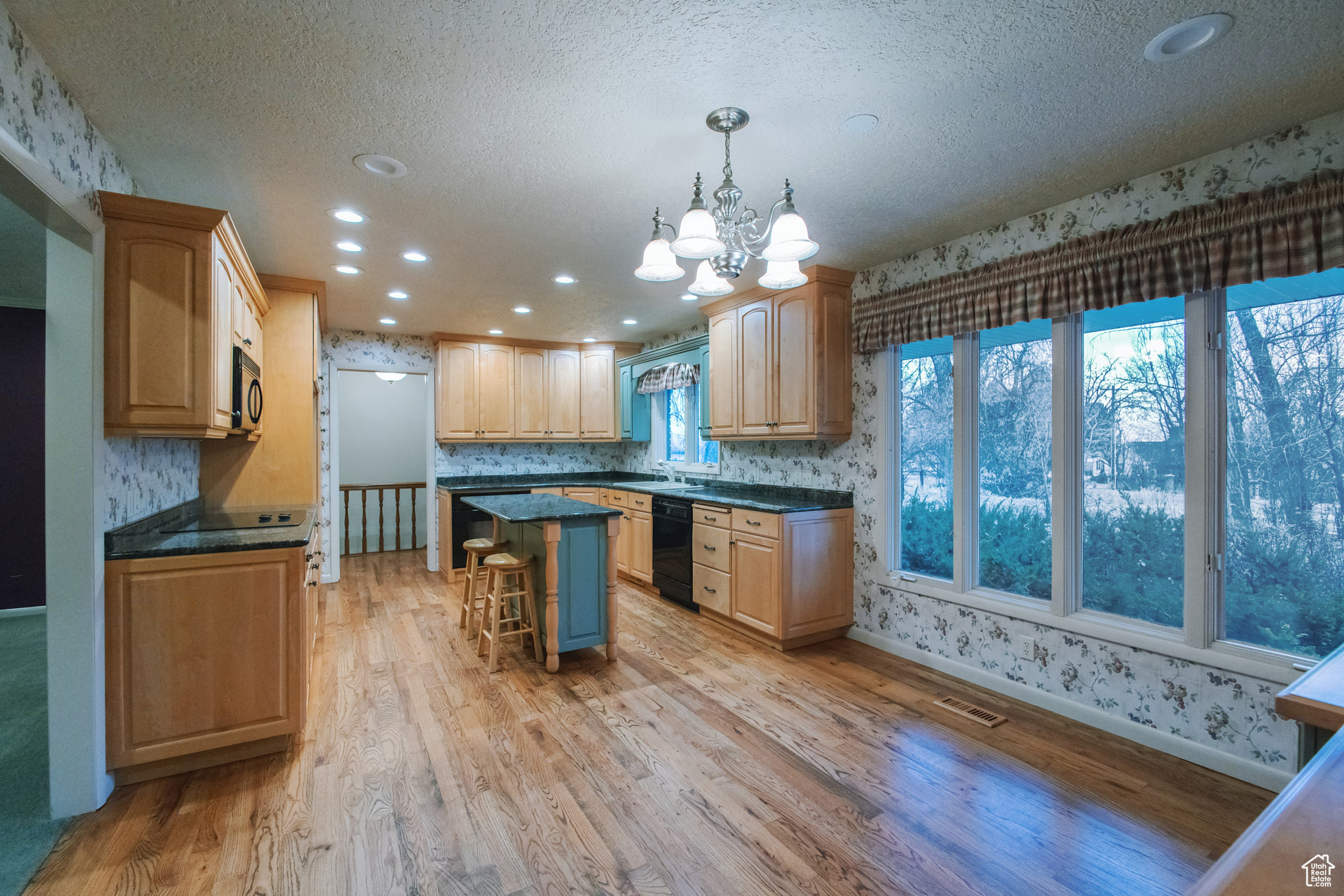 Kitchen with pendant lighting, a kitchen bar, a center island, black appliances, and light wood-type flooring