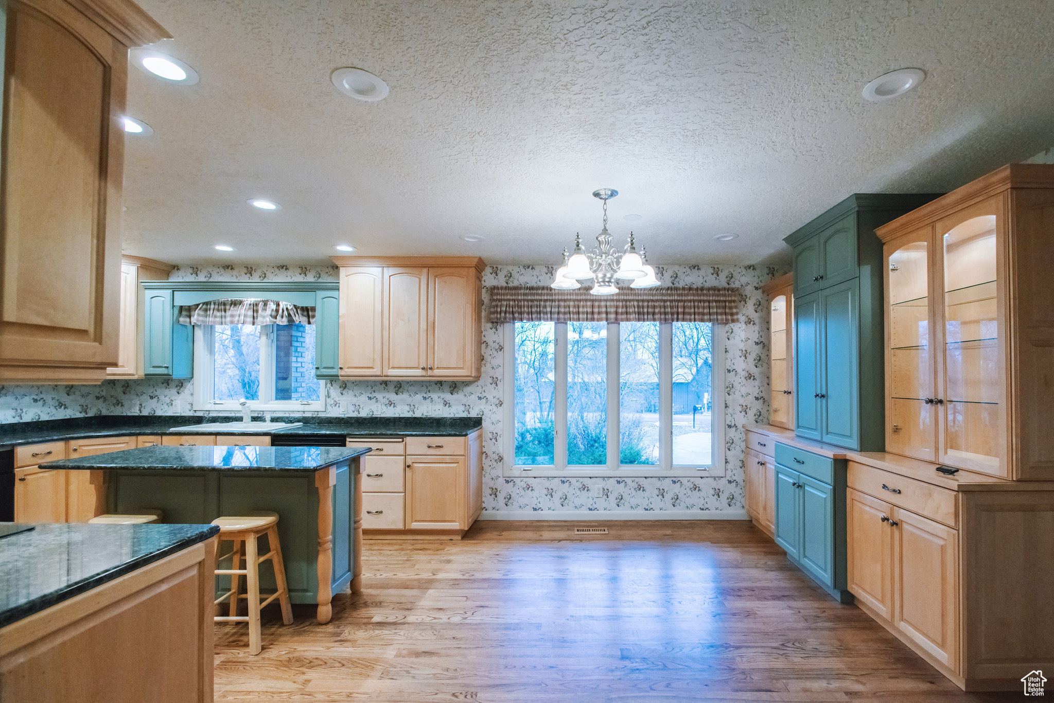 Kitchen with a breakfast bar area, light hardwood / wood-style flooring, dark stone countertops, hanging light fixtures, and a center island