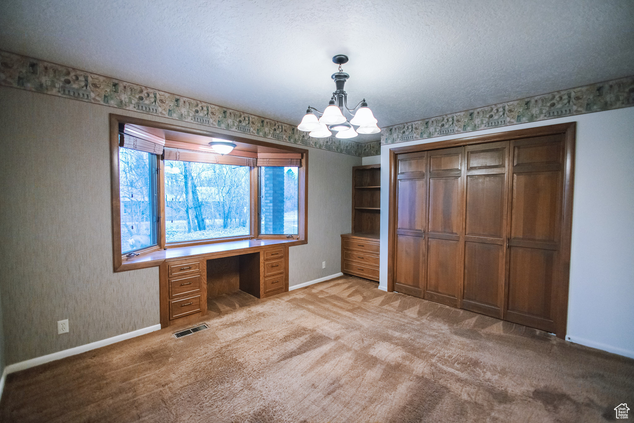 Unfurnished office featuring a notable chandelier, built in desk, light colored carpet, and a textured ceiling