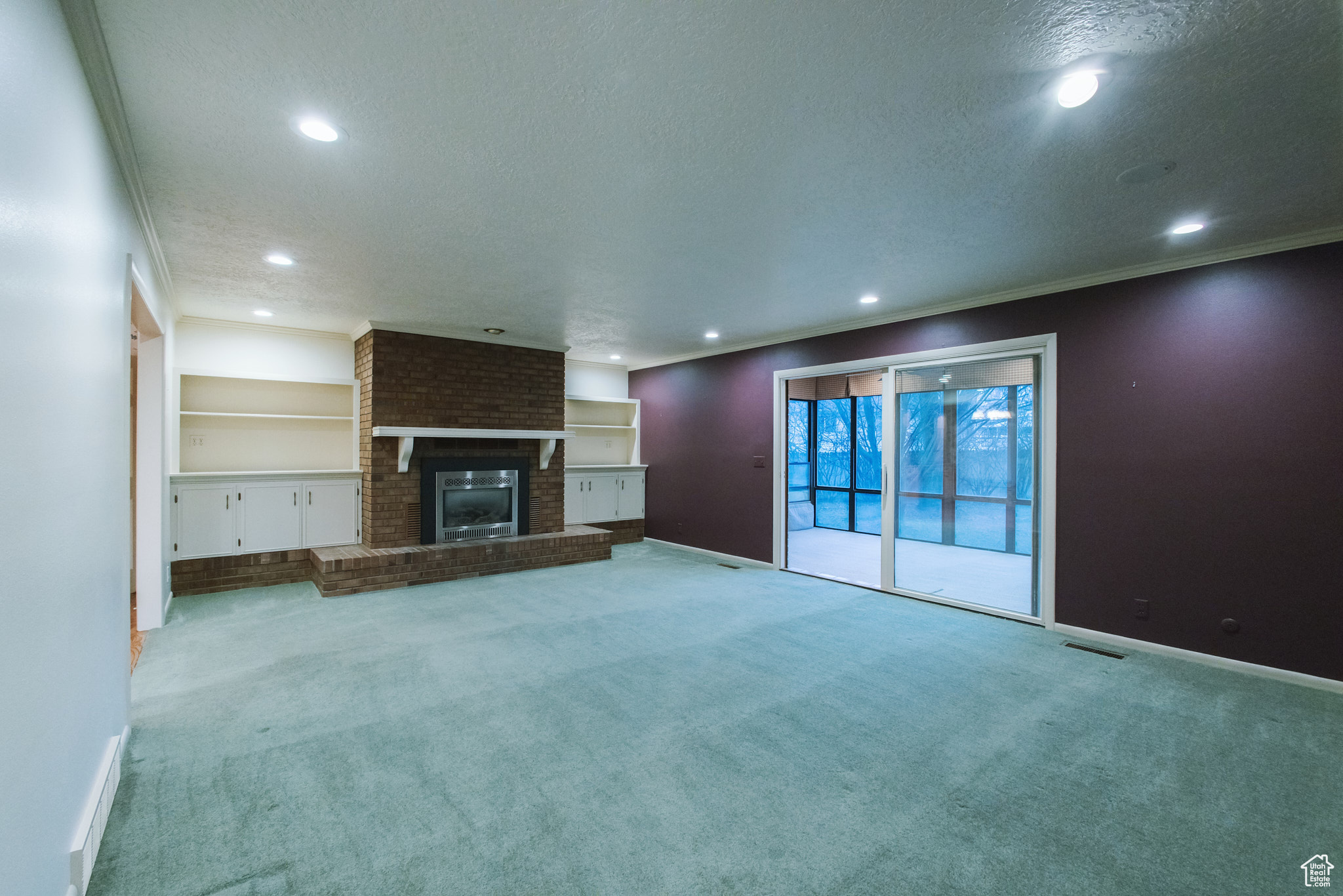 Unfurnished living room featuring light carpet, built in features, and a textured ceiling