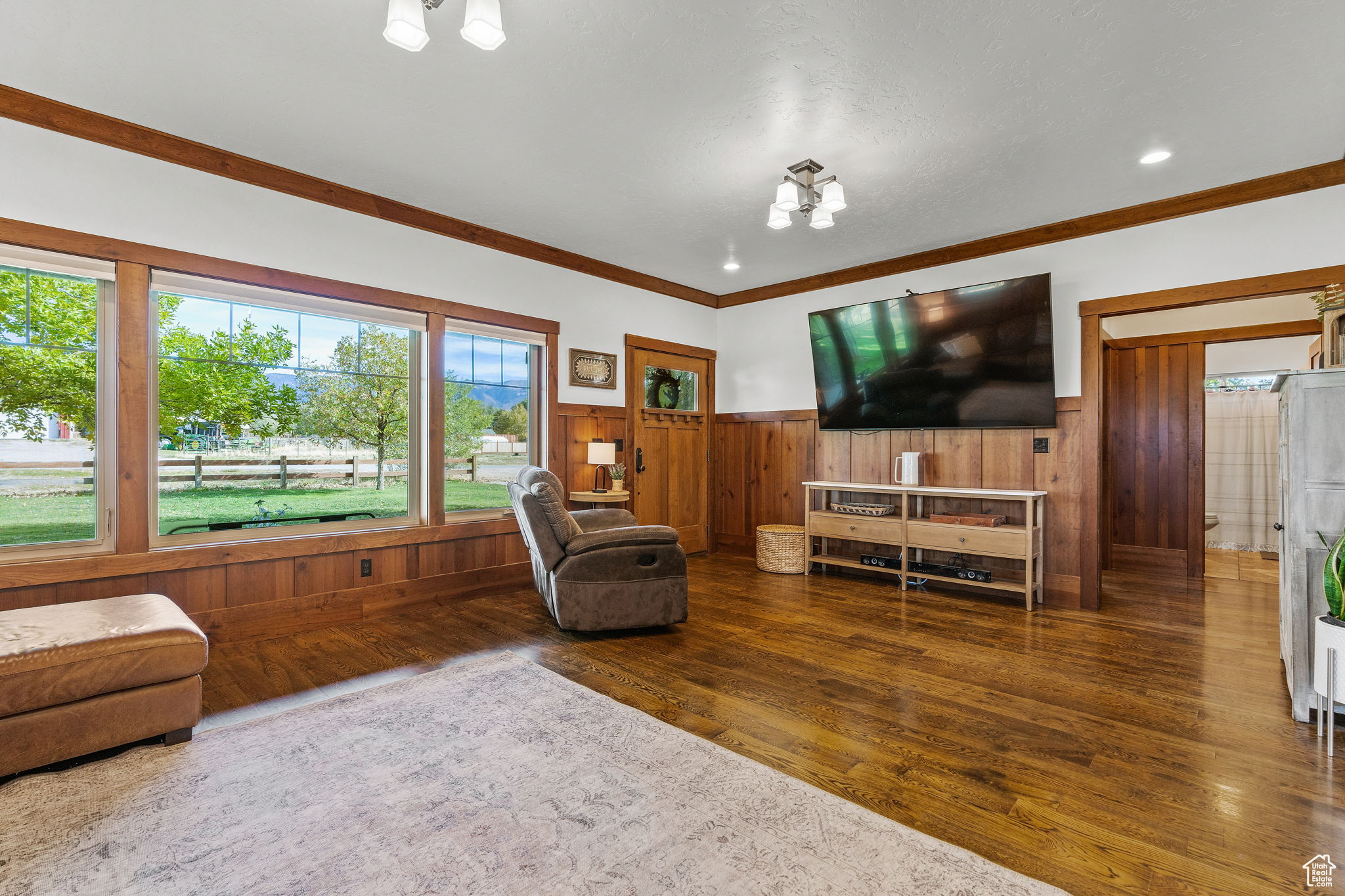 Living room with a notable chandelier, ornamental molding, dark hardwood / wood-style floors, and wood walls