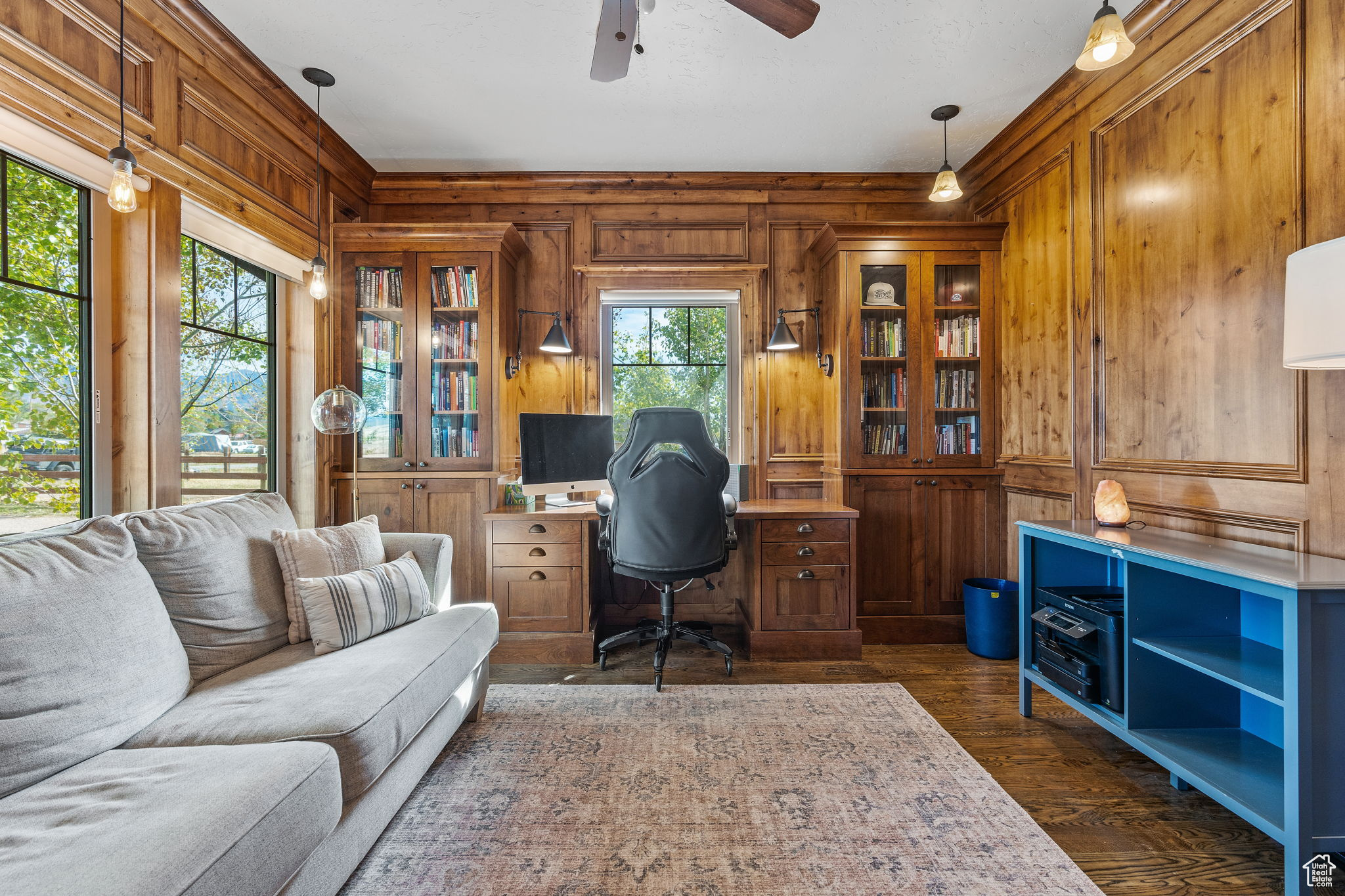 Home office with dark wood-type flooring, ceiling fan, and wood walls
