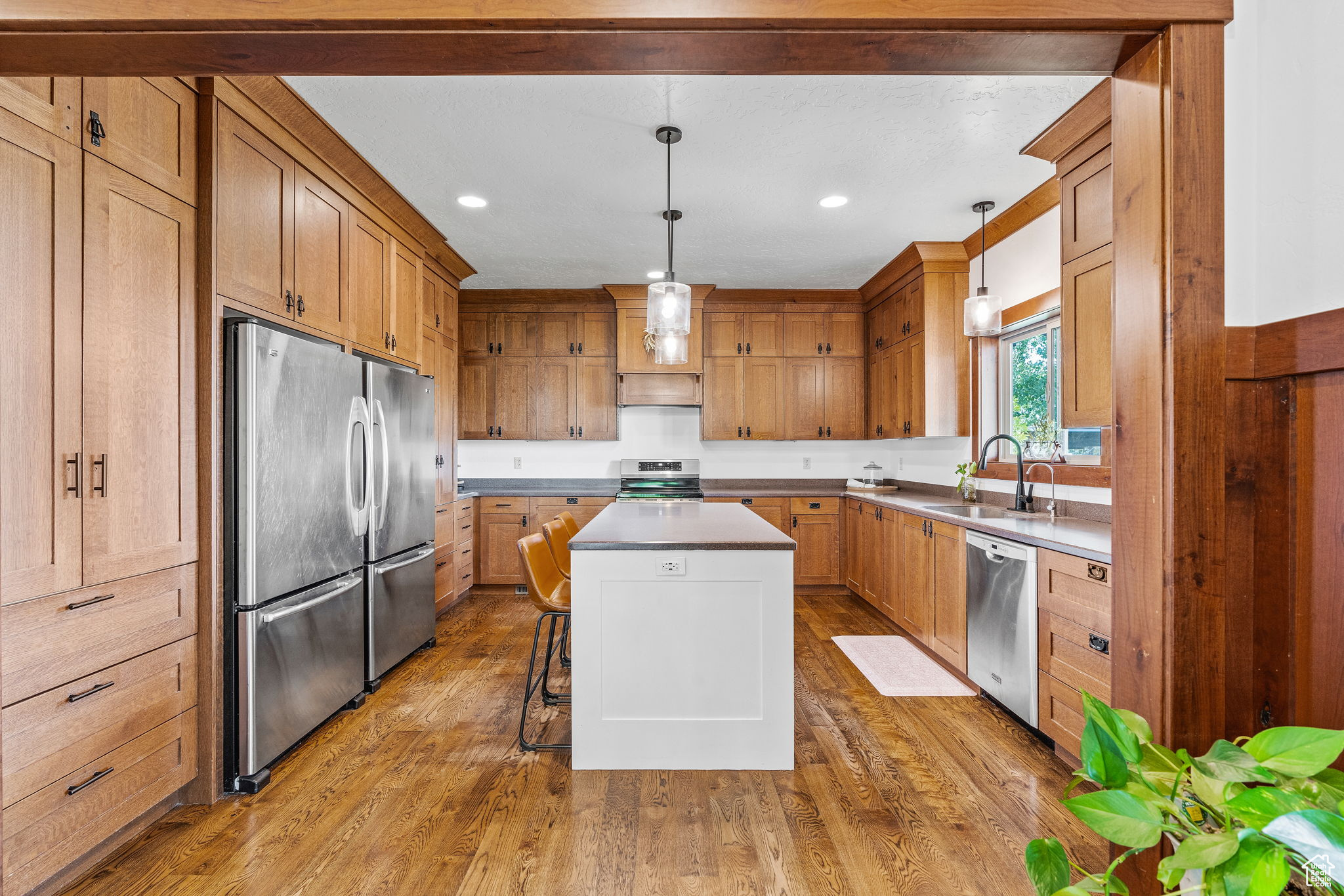 Kitchen with sink, decorative light fixtures, light hardwood / wood-style flooring, appliances with stainless steel finishes, and a kitchen island