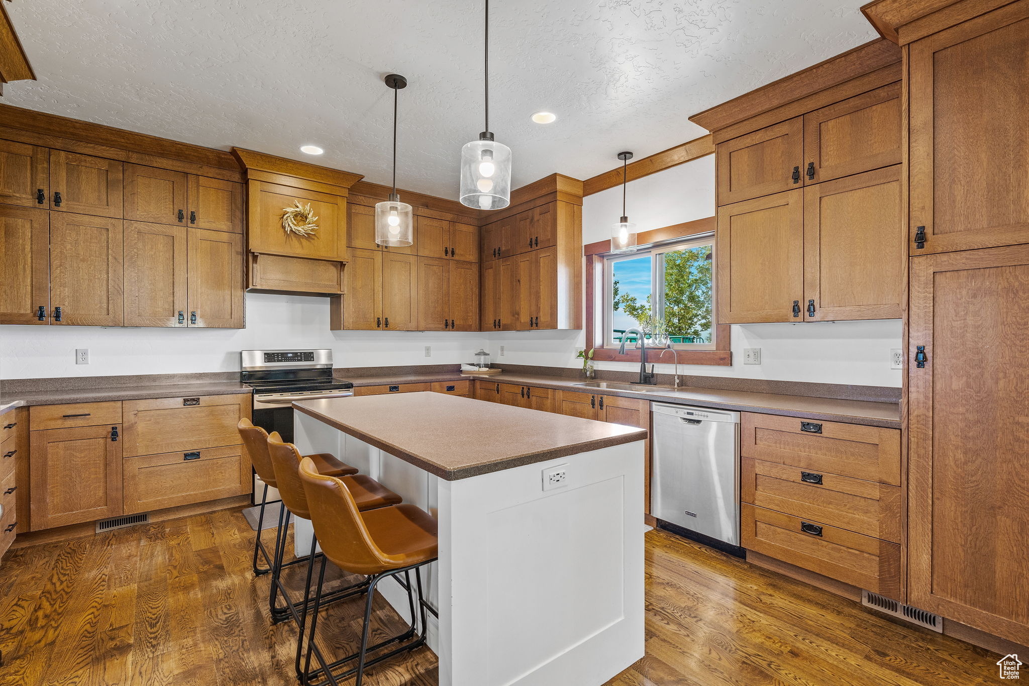 Kitchen with dark wood-type flooring, hanging light fixtures, a kitchen island, stainless steel appliances, and a kitchen bar