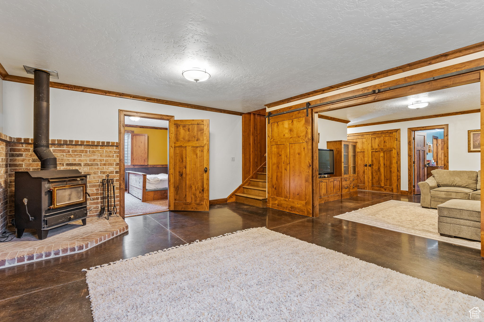Living room with crown molding, a barn door, a wood stove, and a textured ceiling
