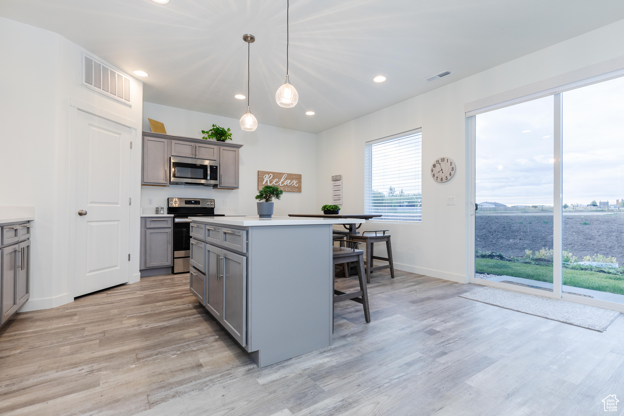 Kitchen with a breakfast bar area, decorative light fixtures, a center island, appliances with stainless steel finishes, and gray cabinets