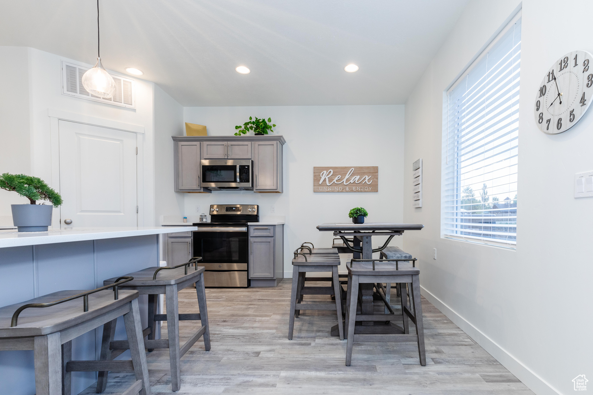 Kitchen with gray cabinets, appliances with stainless steel finishes, light hardwood / wood-style floors, and decorative light fixtures