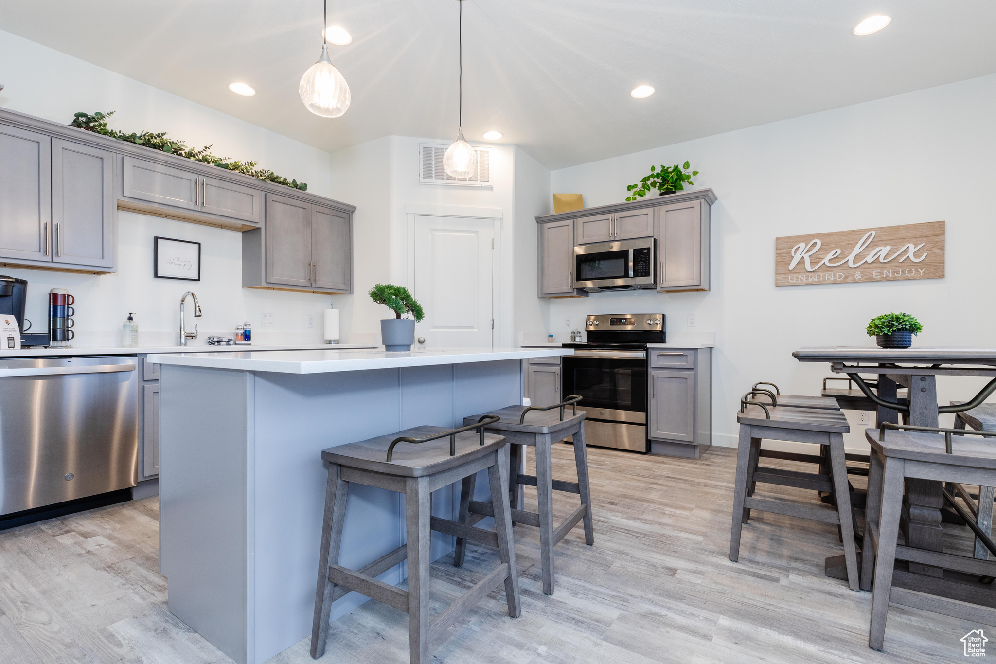 Kitchen featuring sink, light hardwood / wood-style flooring, appliances with stainless steel finishes, gray cabinetry, and decorative light fixtures