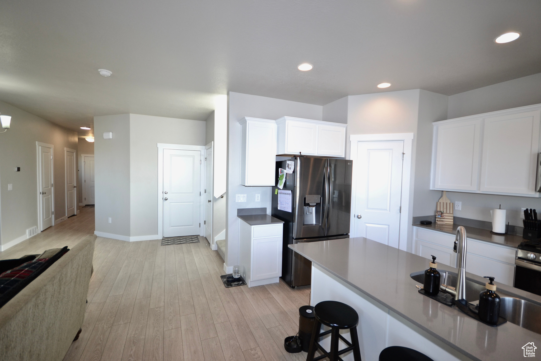 Kitchen with stainless steel refrigerator with ice dispenser, sink, a breakfast bar area, light wood-type flooring, and white cabinets