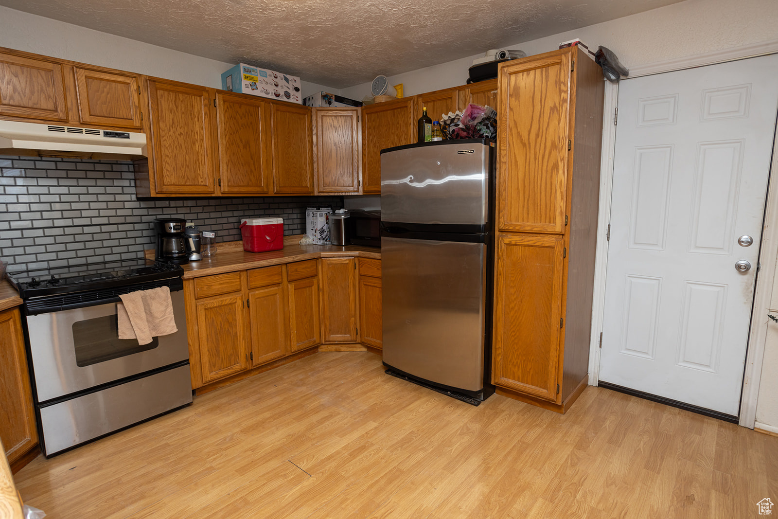 Kitchen with stainless steel appliances, backsplash, a textured ceiling, and light hardwood / wood-style flooring