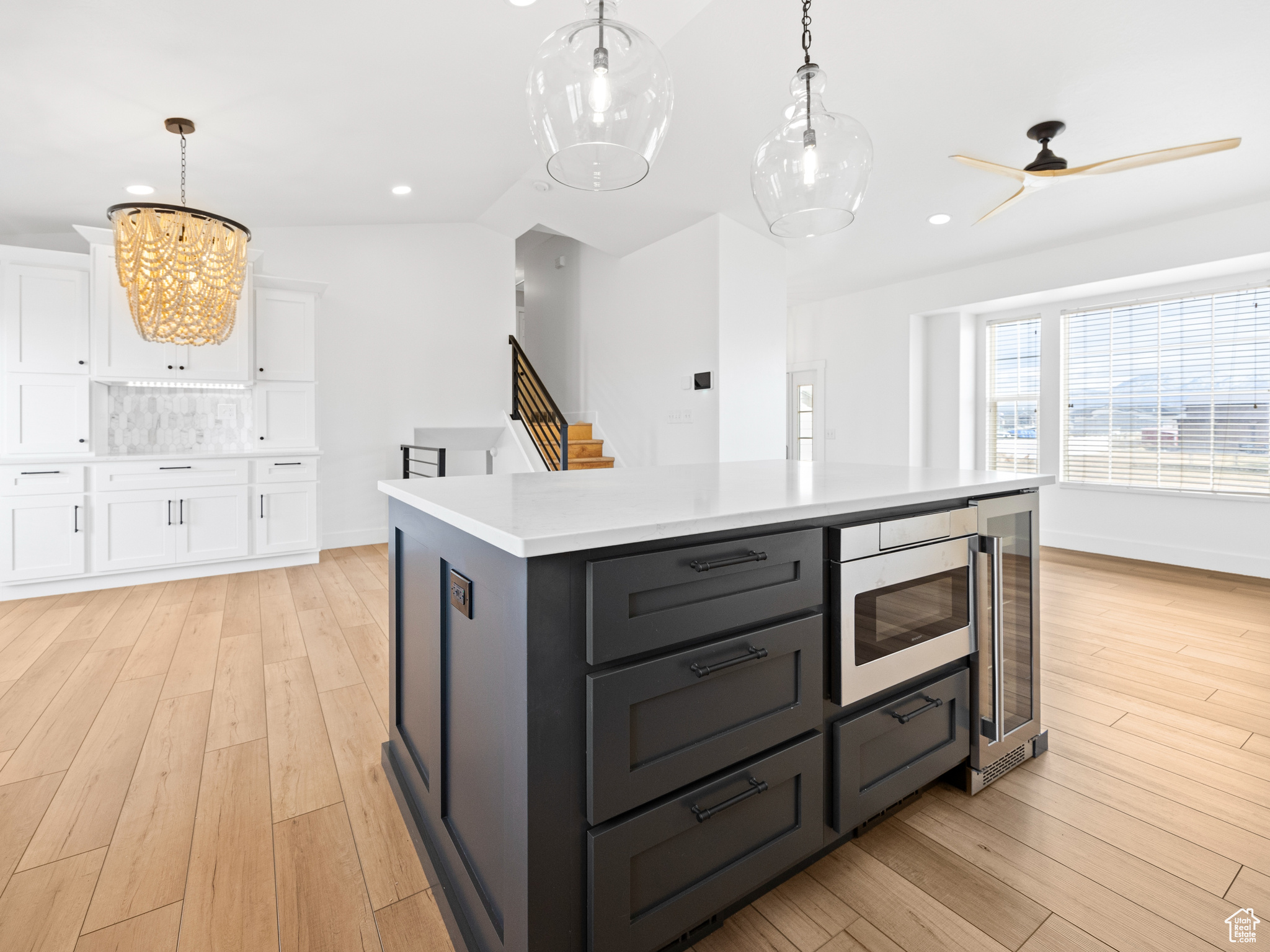 Kitchen with pendant lighting, stainless steel microwave, white cabinets, a center island, and light hardwood / wood-style floors