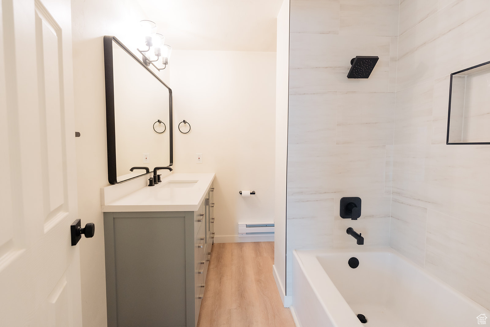 Bathroom featuring vanity, wood-type flooring, tiled shower / bath, and baseboard heating