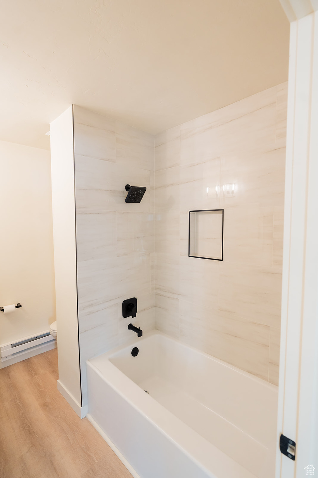 Bathroom featuring hardwood / wood-style flooring, toilet, tiled shower / bath combo, and a baseboard heating unit