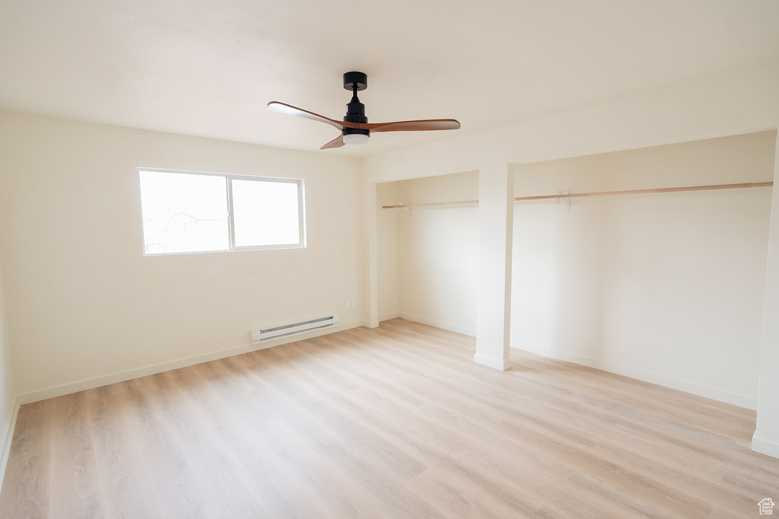 Unfurnished bedroom featuring ceiling fan, two closets, baseboard heating, and light hardwood / wood-style floors