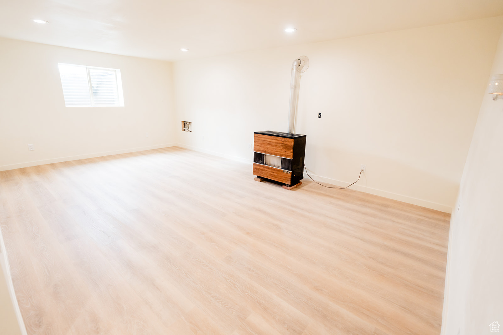 Unfurnished room featuring a wood stove and light wood-type flooring