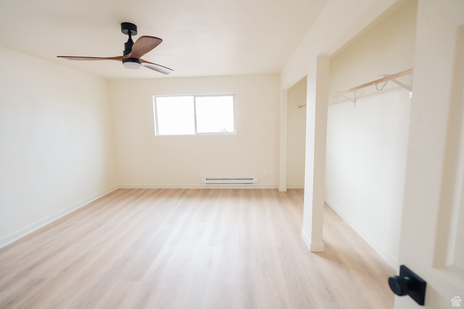 Unfurnished bedroom with ceiling fan, baseboard heating, and light hardwood / wood-style floors