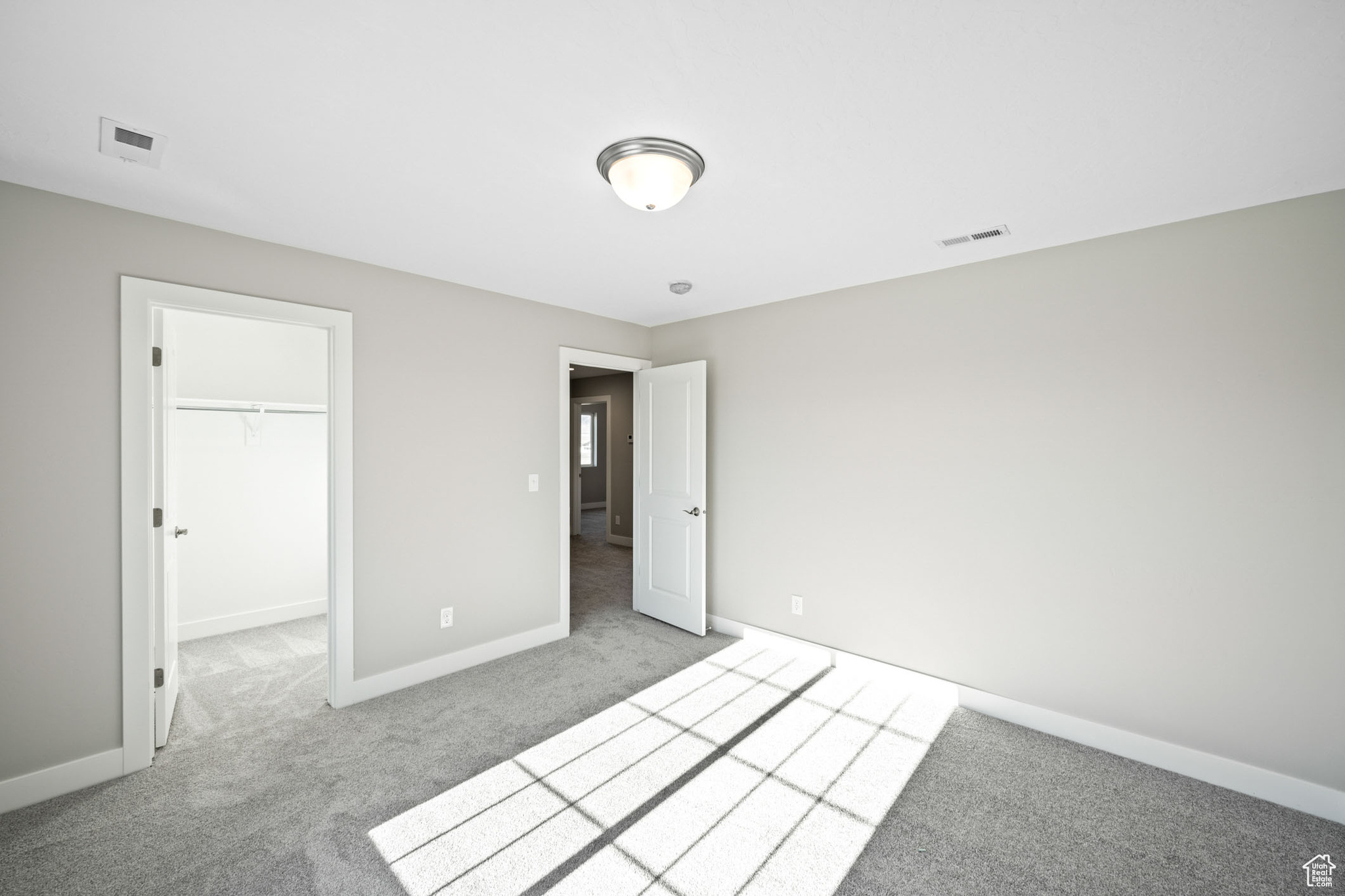 Unfurnished bedroom with a walk in closet, a closet, and light carpet
