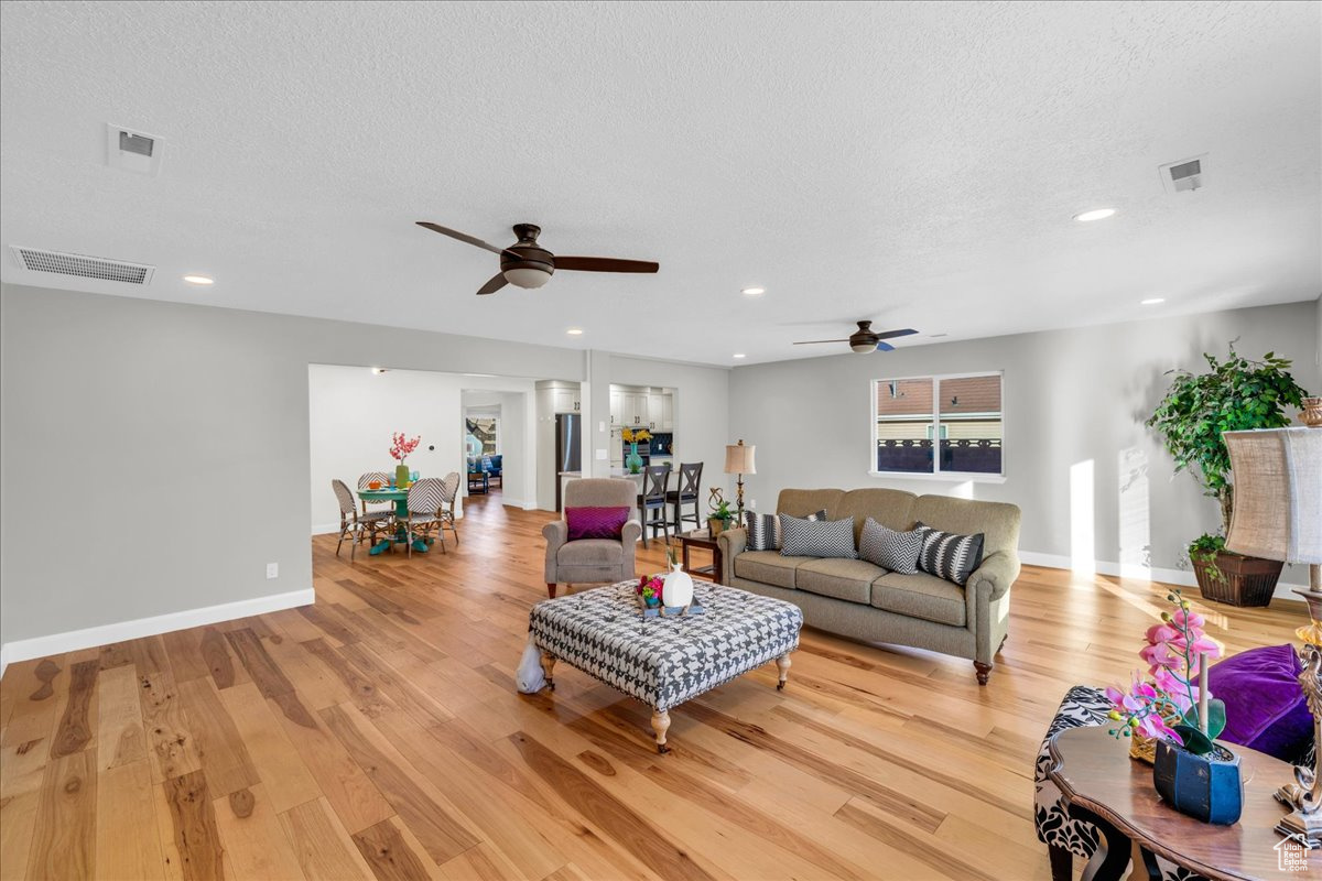 Living room featuring ceiling fan, a textured ceiling, and light hardwood / wood-style flooring