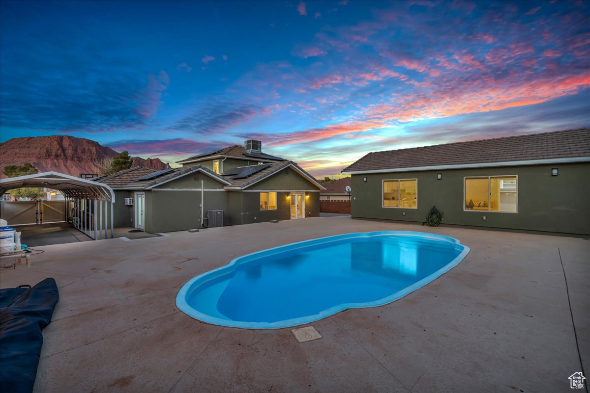 Pool at dusk featuring a carport, a mountain view, and a patio area
