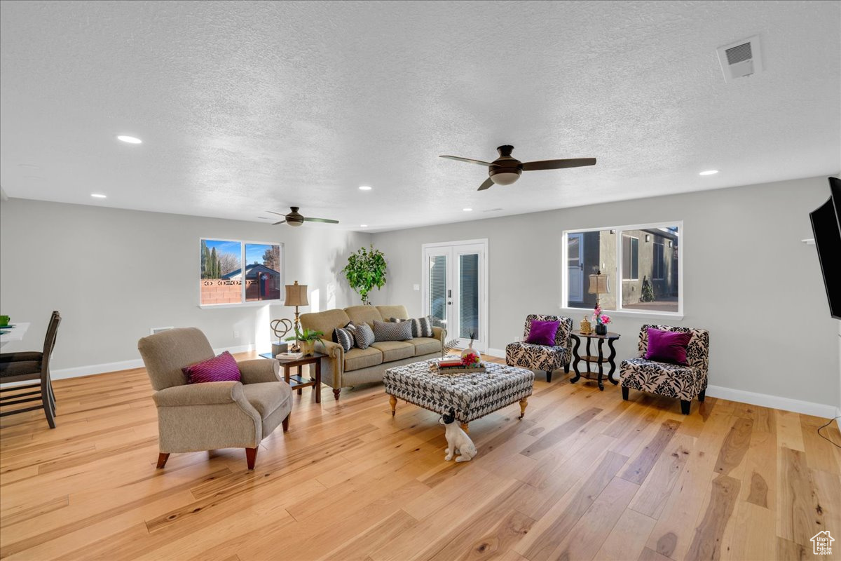 Living room with ceiling fan, french doors, a textured ceiling, and light wood-type flooring