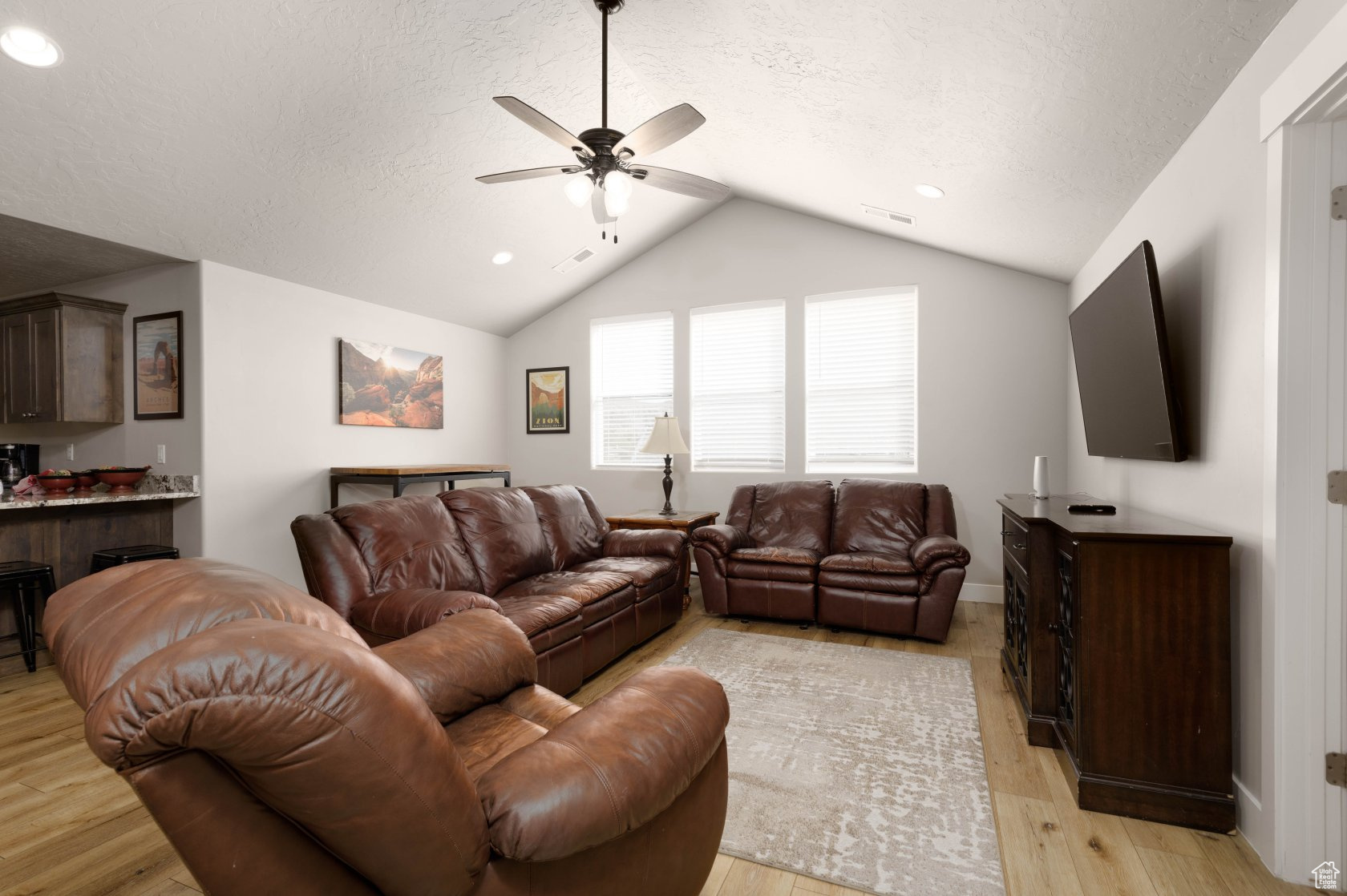 Living room with lofted ceiling, ceiling fan, light hardwood / wood-style flooring, and a textured ceiling
