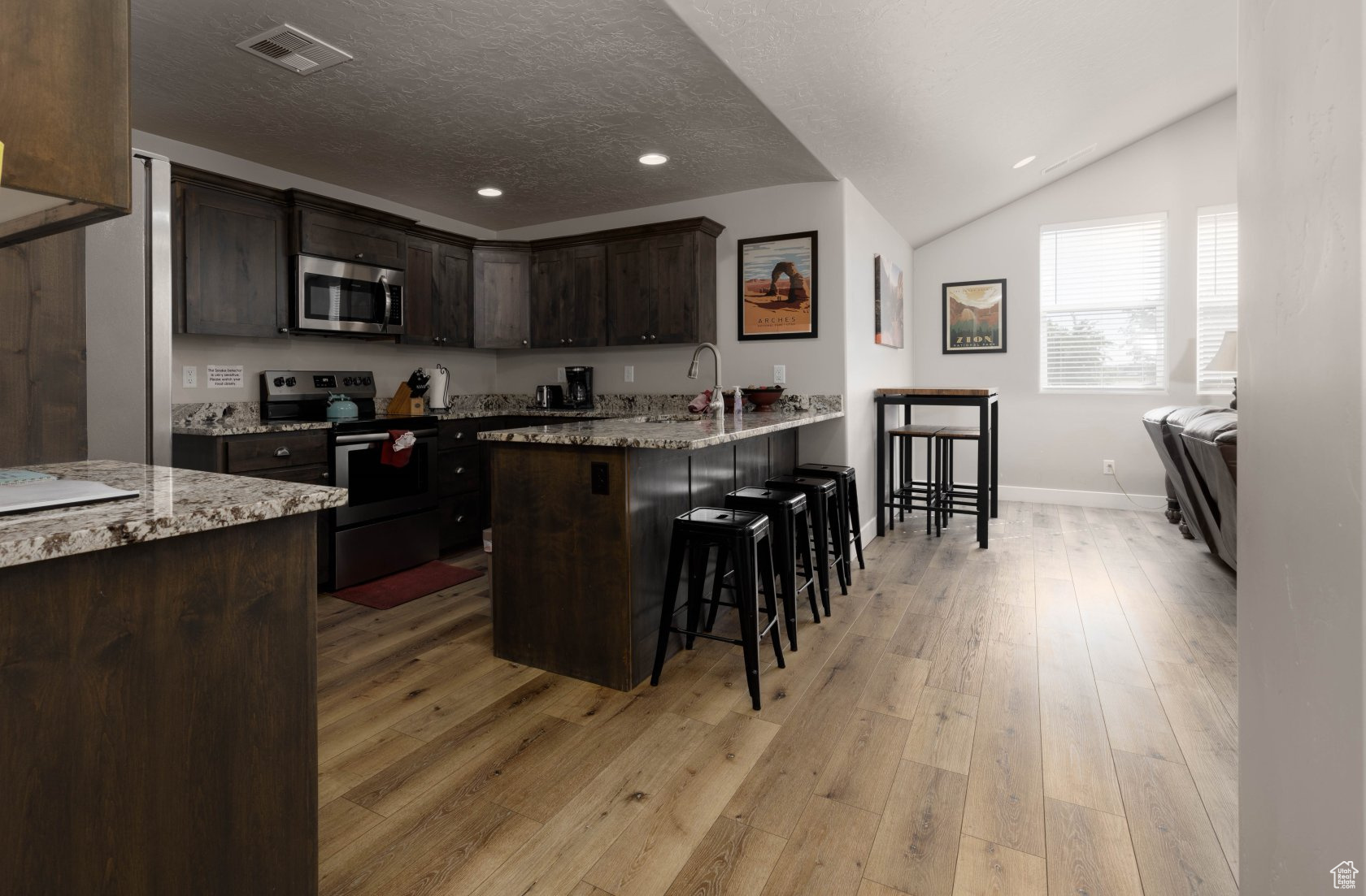 Kitchen featuring a breakfast bar area, appliances with stainless steel finishes, dark brown cabinetry, light stone counters, and light wood-type flooring