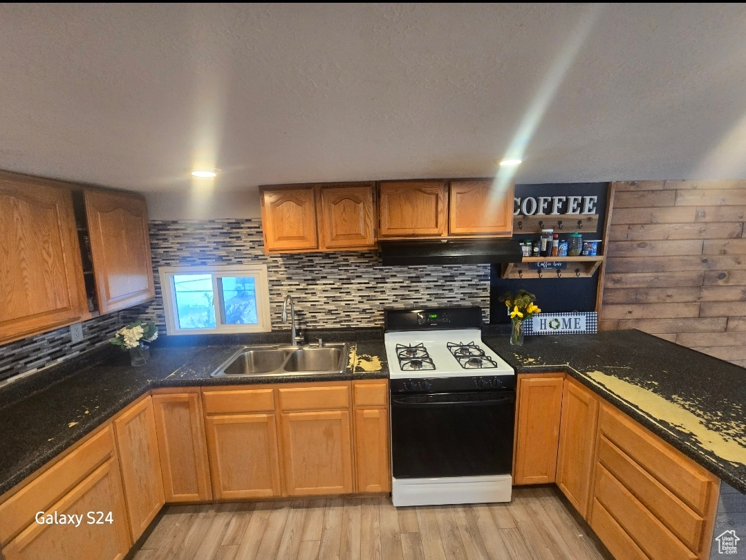 Kitchen with tasteful backsplash, range with gas stovetop, sink, and light wood-type flooring