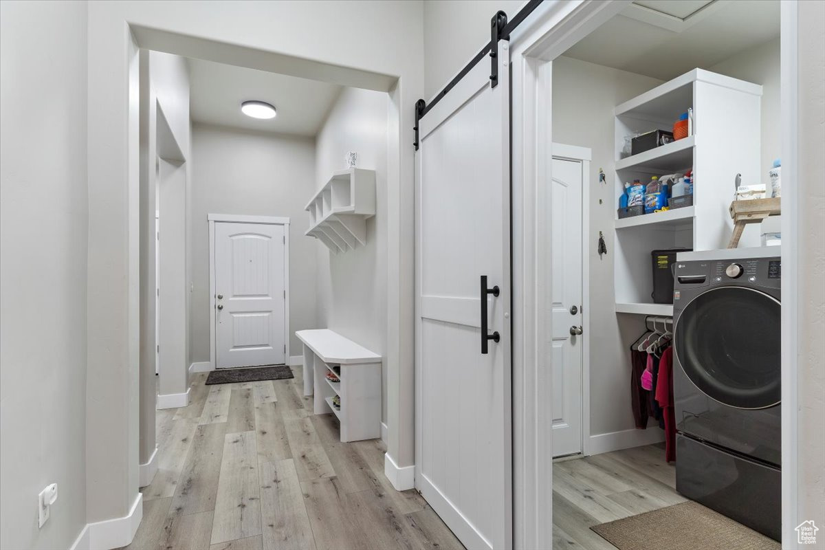 Laundry room with a barn door, washer / dryer, and light hardwood / wood-style flooring