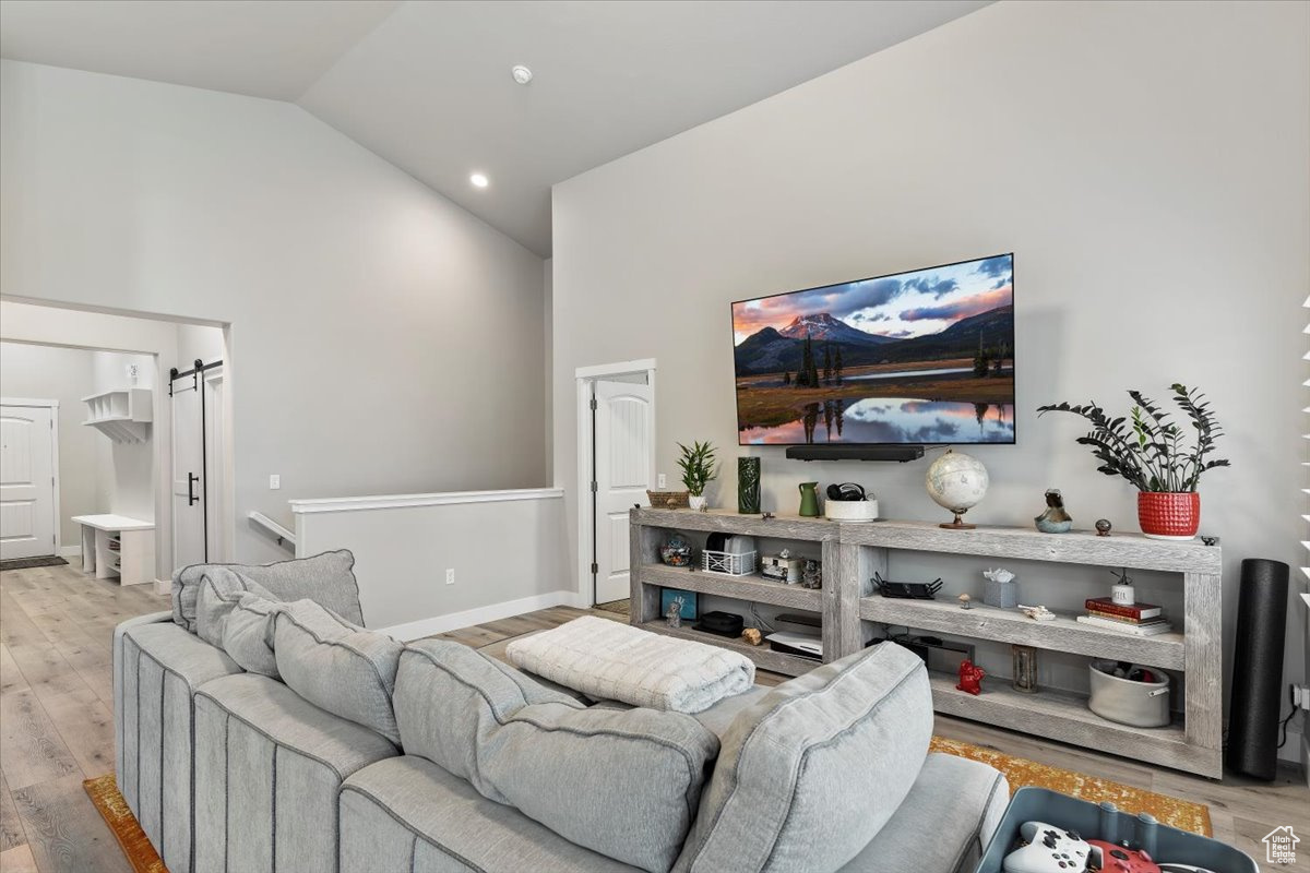 Living room featuring high vaulted ceiling, a barn door, and light wood-type flooring