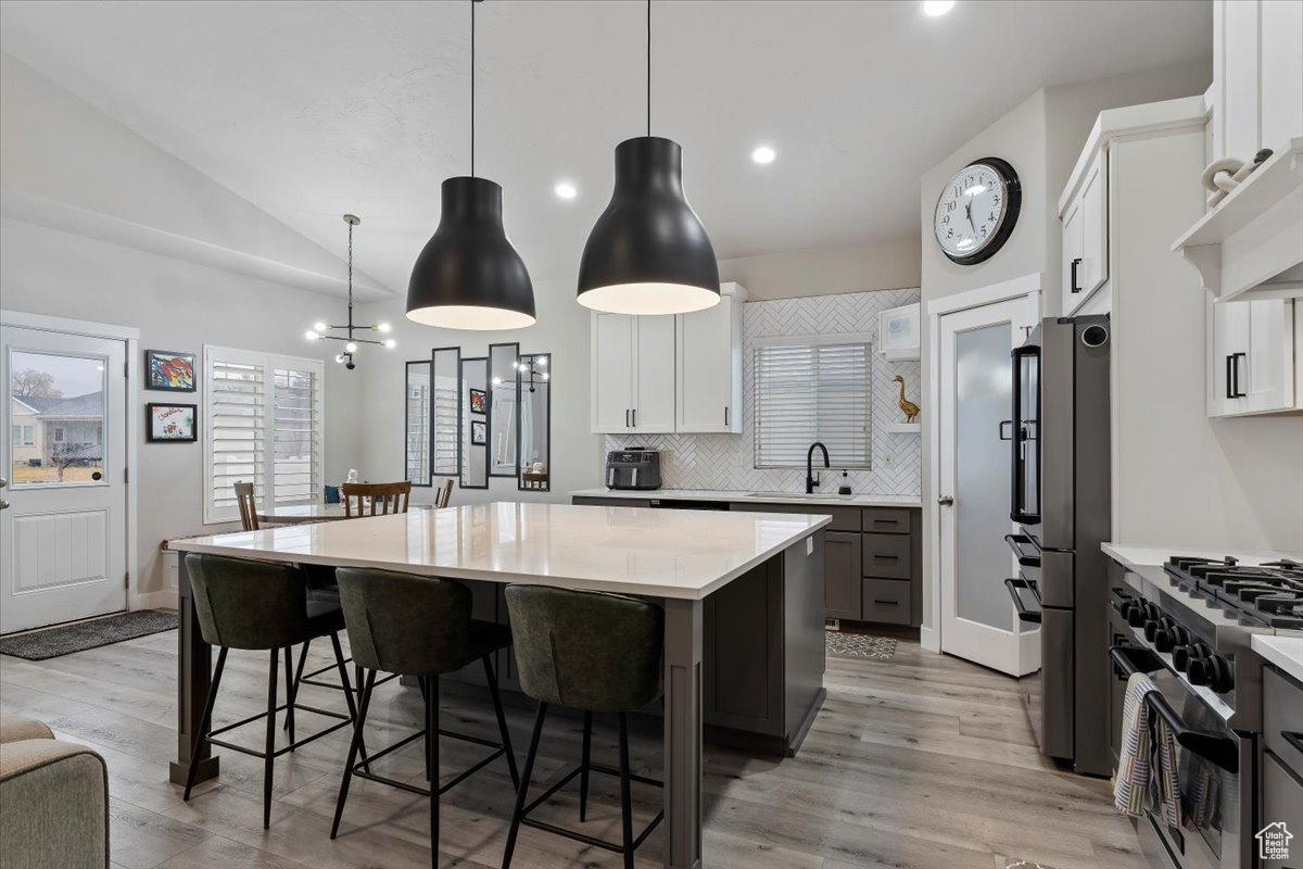 Kitchen featuring sink, stainless steel appliances, white cabinets, a kitchen island, and decorative light fixtures