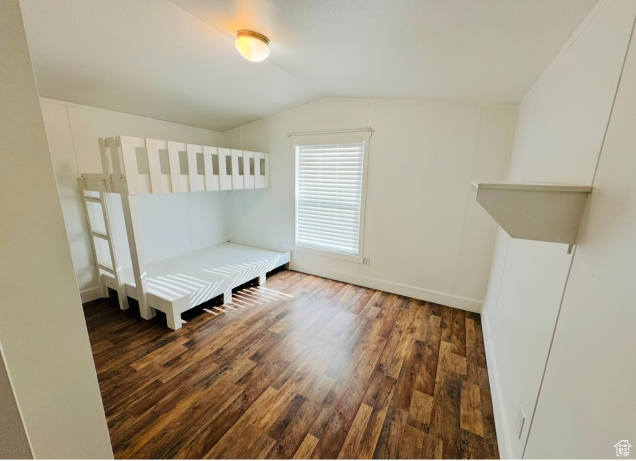 Unfurnished bedroom with lofted ceiling and dark wood-type flooring