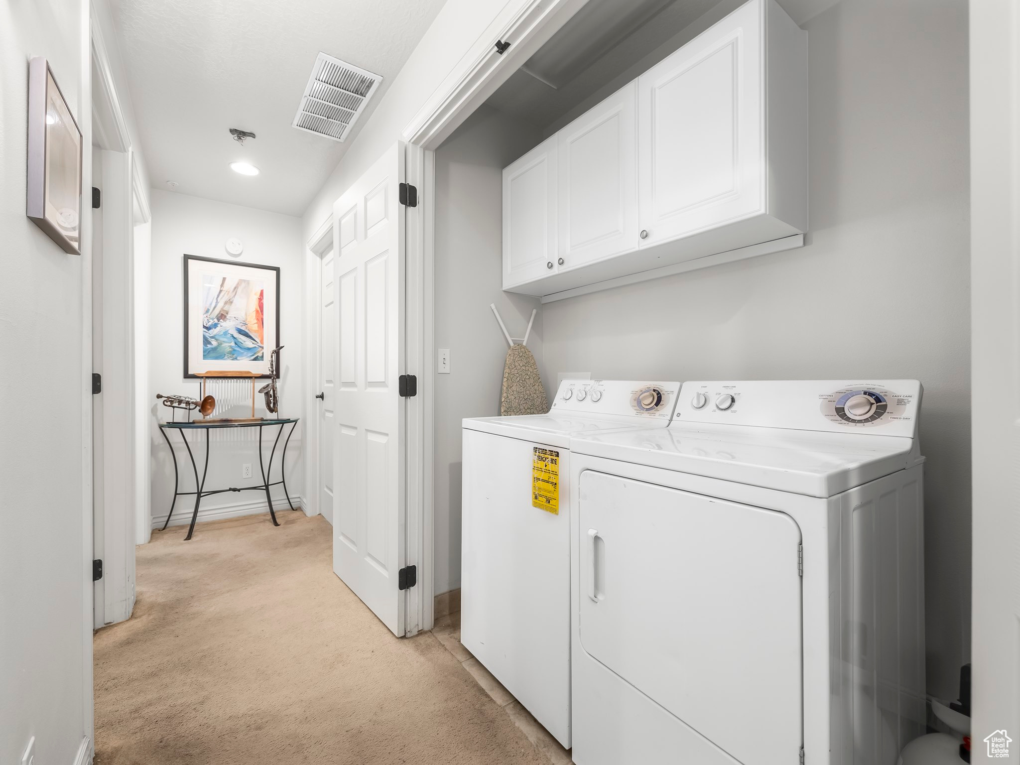 Clothes washing area with light carpet, washing machine and dryer, and cabinets
