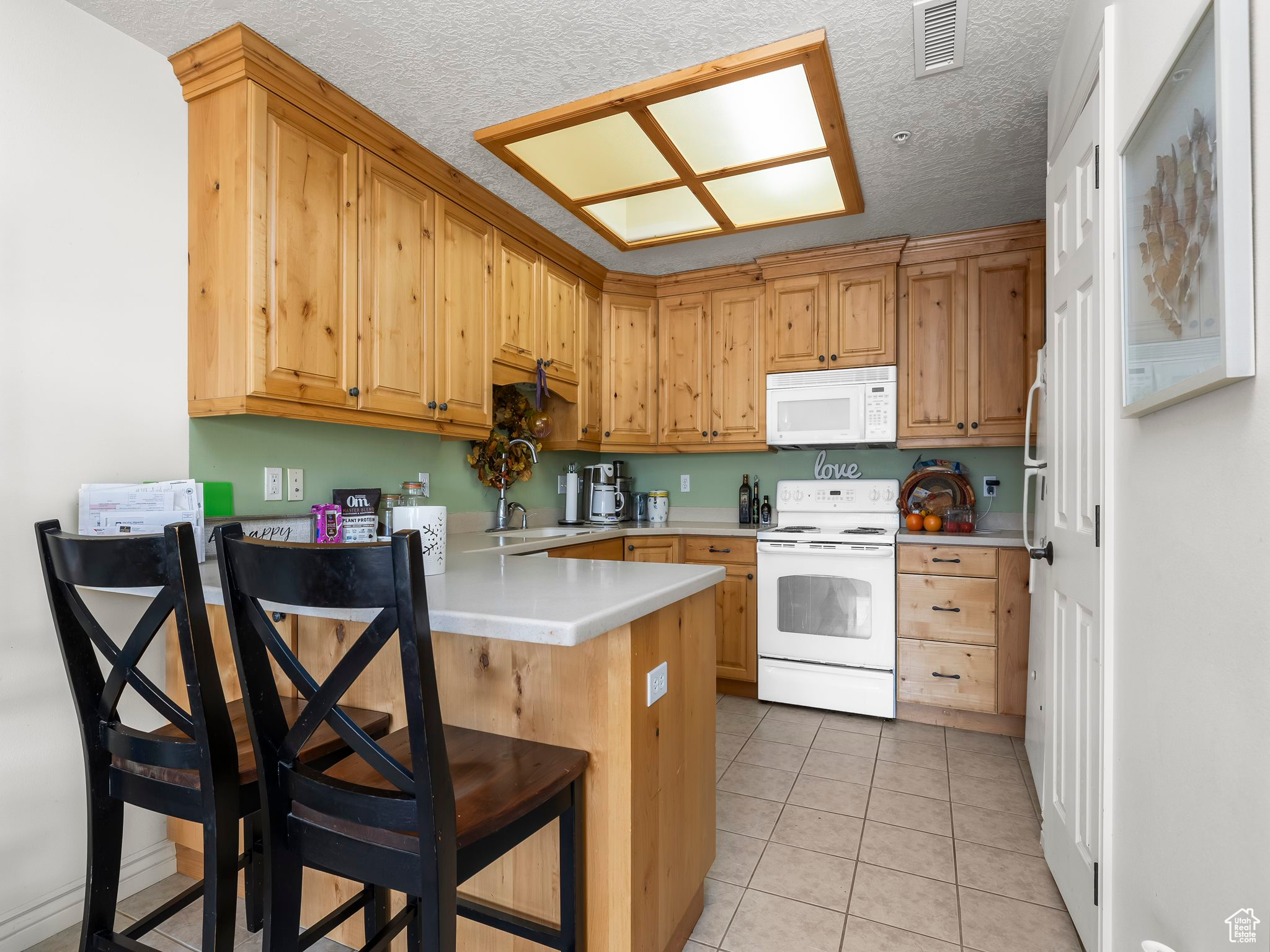 Kitchen featuring light tile patterned flooring, a kitchen bar, white appliances, kitchen peninsula, and a textured ceiling